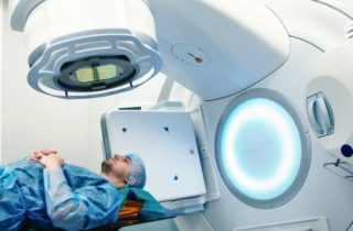 man with a cap lays on a hospital bed waiting to receive radiation treatment