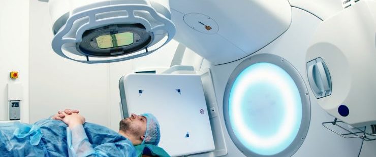 man with a cap lays on a hospital bed waiting to receive radiation treatment