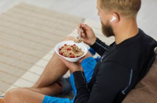 back of a man sitting on a coach with airpods eating a bowl of oats and fruit