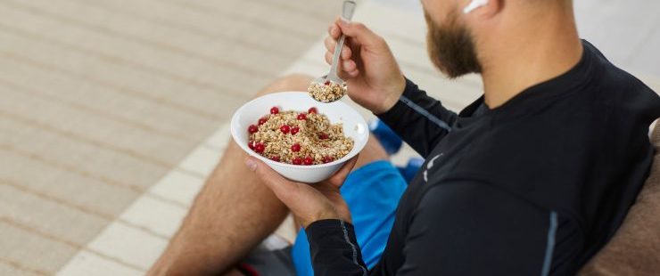 back of a man sitting on a coach with airpods eating a bowl of oats and fruit